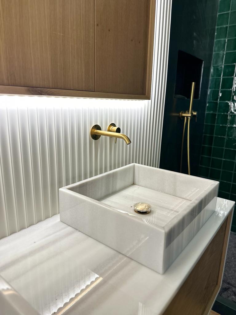 Lavatório quadrado em mármore branco com torneira dourada